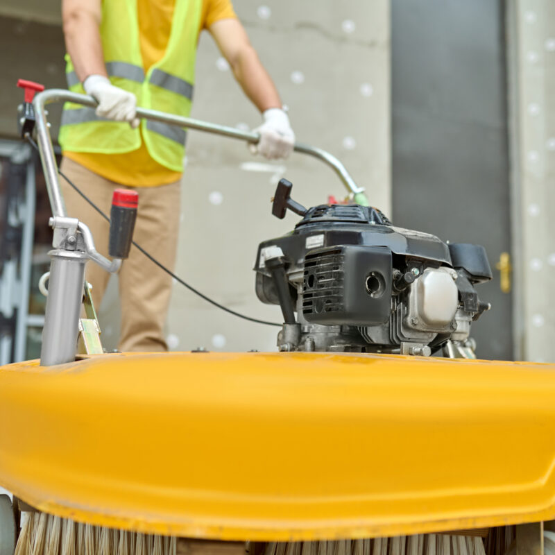 Cropped photo of a worker cleaning the outdoor floor tiles with a street sweeping machine